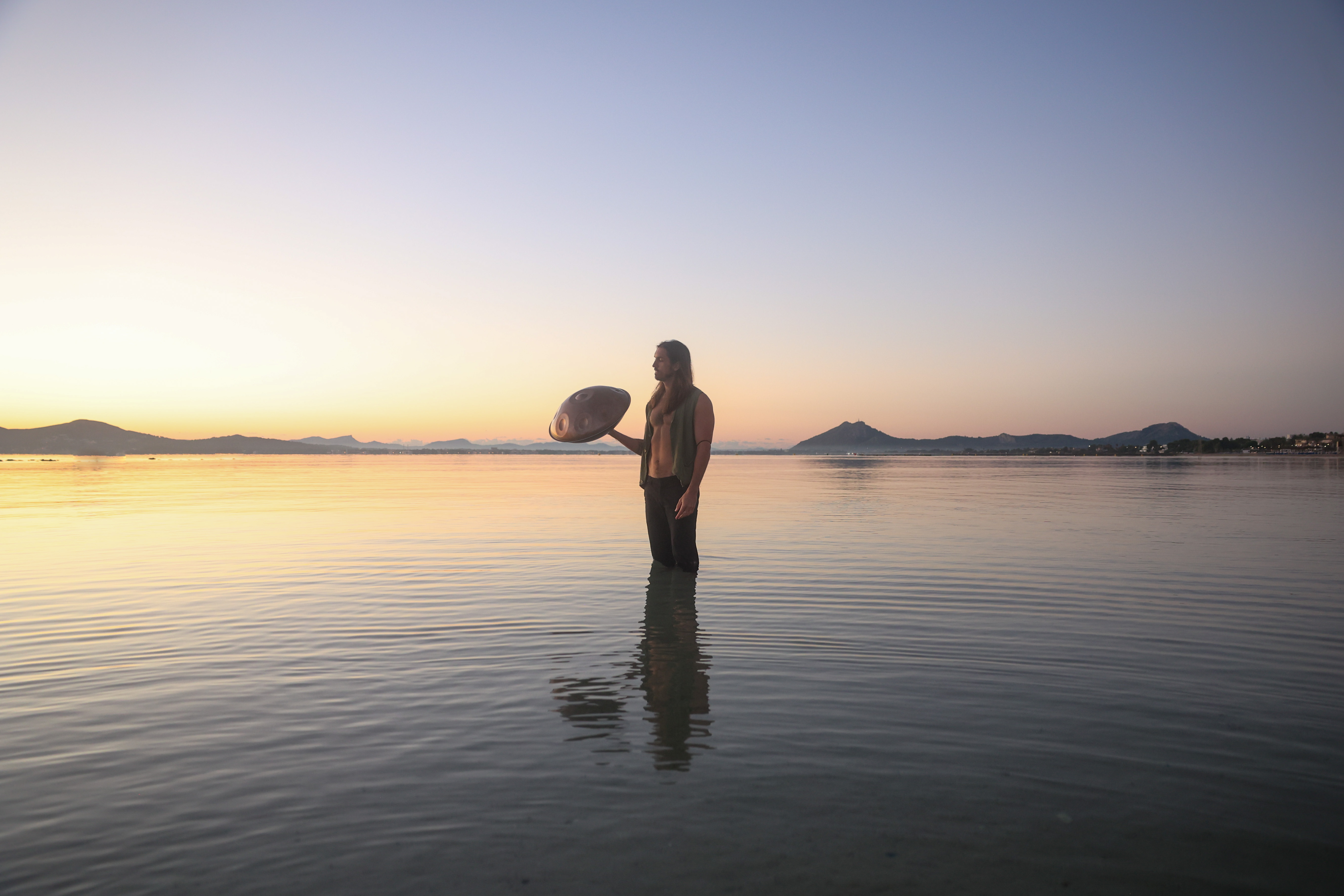 Sandy holding a handpan by a lake at sunset